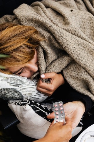 Donna a letto sotto le coperte che prende in mano delle pastiglie Donna a letto sotto le coperte che prende in mano delle pastiglie